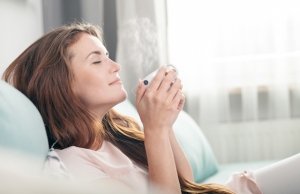 Young woman sitting on couch at home and drinking coffee, casual style indoor shoot. perpetually single