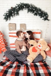 Loving young couple sitting on floor by christmas tree at christmas morning, caressing.